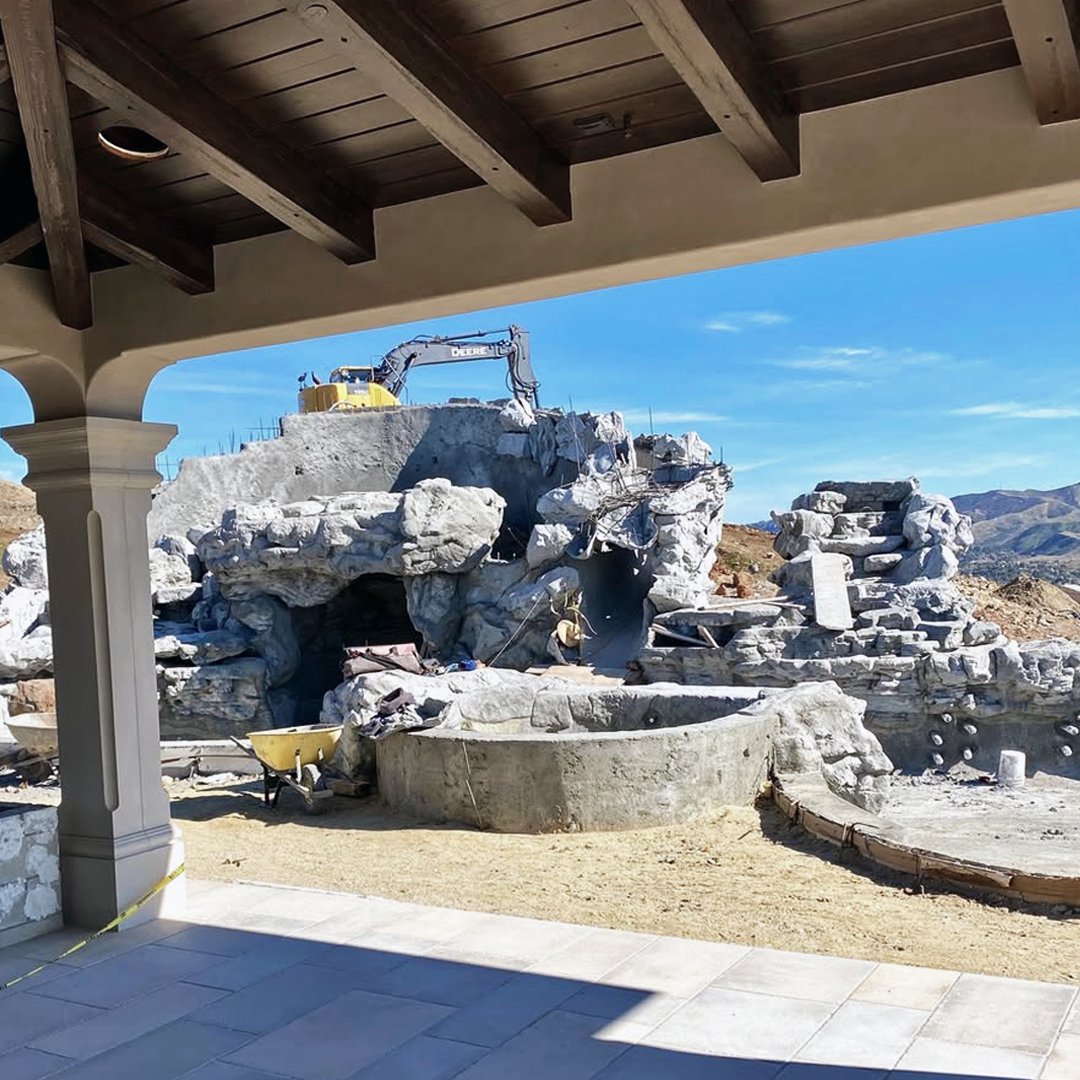 Simi Valley pool under construction — hand-sculpted gunite rockwork being shaped by excavator on a raw hilltop